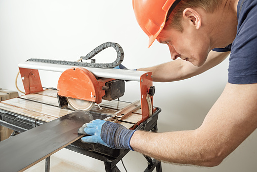 The worker is cutting a ceramic tile on a wet cutter saw  machine.