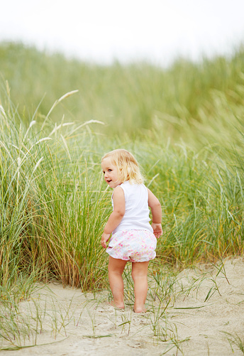 Adorable littl girl walking through tall grass while having fun on a sandy beach on a sunny day