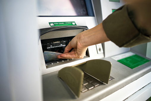 Young woman using the card for withdrawing the cash in the ATM.