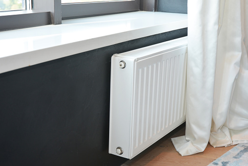 White radiator heating with thermostat for energy saving in luxury bedroom with black walls and white sunblind, curtain.