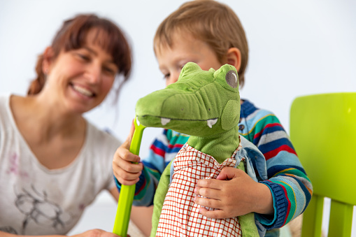 Little Boy Practicing Correct Teeth Brushing on Crocodile Stuffed Toy with his Supportive Mother