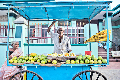 Kanniyakumari, India - September 13, 2013: A local street vendor in a blue cart, toiling hard for selling fruit salad, mangoes and corns.