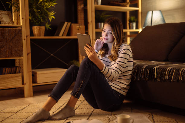 istock Young smiling woman using digital tablet in a living room at night 1226035623