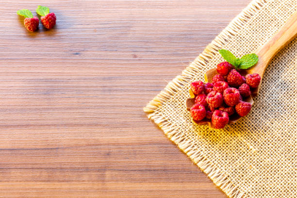 Spoon with raspberry and bowl with raspberry jam on wooden background