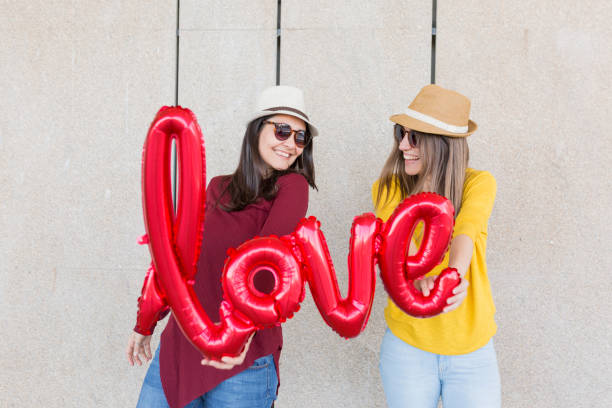 istock two beautiful young women having fun outdoors with a red balloon with a love word shape. Casual clothing. They are wearing hats and modern sunglasses. LIfestyle outdoors 1226043687