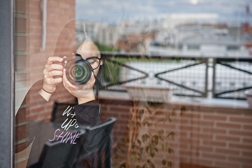 Teenage girl takes photos with her camera through the window at home
