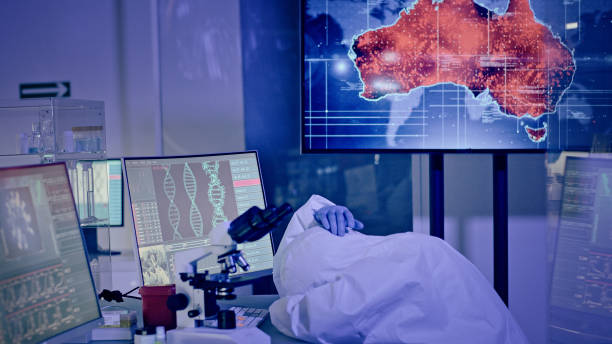 Exhausted scientist in futuristic laboratory. Sleeping on the desk. Infected Australia Modern laboratory interior. Coronavirus control - map of virus occurence. Red alert human genome map stock pictures, royalty-free photos & images