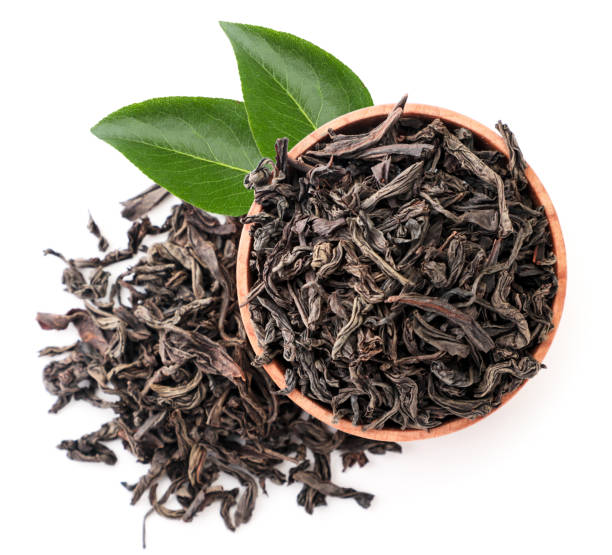 Black tea in a wooden plate with green leaves close-up on a white, isolated. The view from top Black tea in a wooden plate with green leaves close-up on a white background, isolated. The view from top black tea stock pictures, royalty-free photos & images