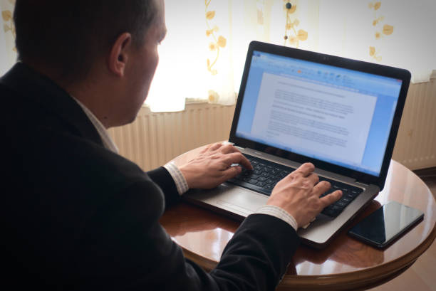 Senior academician working from home writing essay from his laptop on a table stock photo