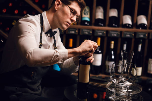 istock Bartender opening wine bottle with corkscrew in restaurant with wine shelves. 1226058161