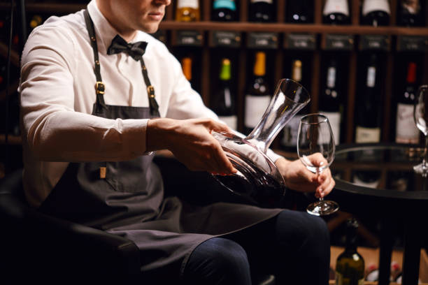 istock Sommelier pouring red wine from bottle into decanter at table in restaurant 1226058405