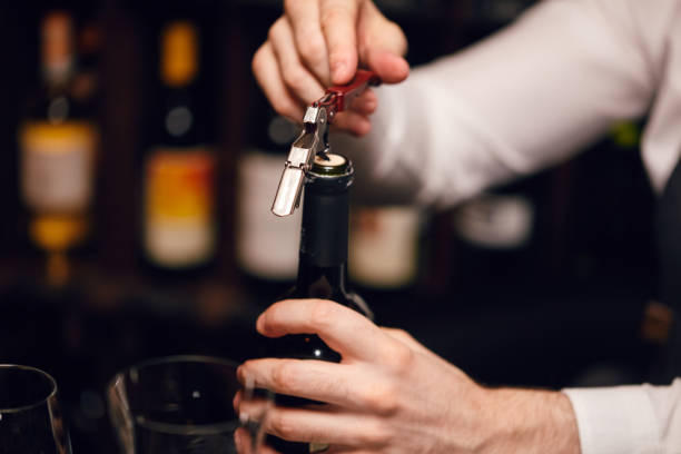 barista che apre una bottiglia di vino con cavatappi al ristorante con scaffali per vini. - wine cork wine bottle bottle foto e immagini stock