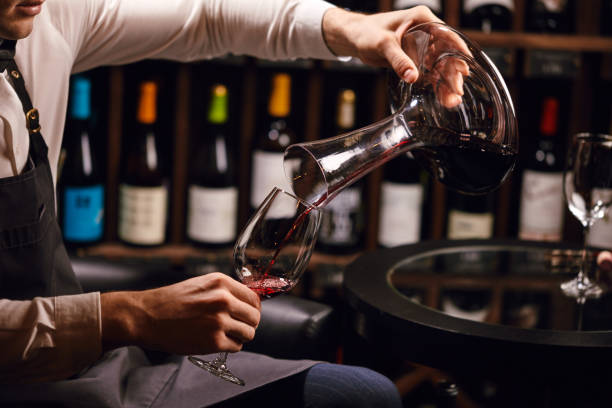 istock Sommelier pouring red wine from bottle into decanter at table in restaurant 1226059010