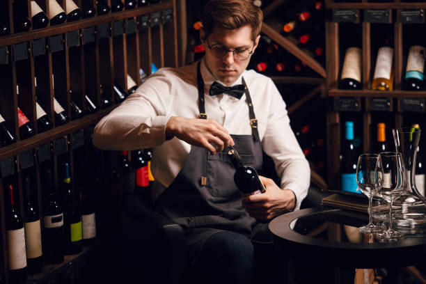 istock Bartender opening wine bottle with corkscrew in restaurant with wine shelves. 1226059042