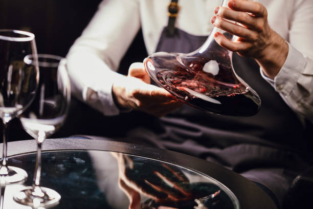 Sommelier pouring red wine from bottle into decanter at table in restaurant Cropped view of professional sommelier holding mixing bowl with red wine in hands over the table in wine restaurant. sommelier photos stock pictures, royalty-free photos & images