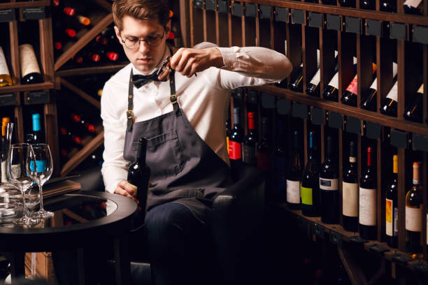 istock Bartender opening wine bottle with corkscrew in restaurant with wine shelves. 1226059369