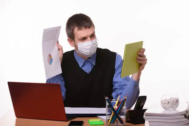 Photo of A man in a medical mask shows a paper document with graphs to a virtual interlocutor
