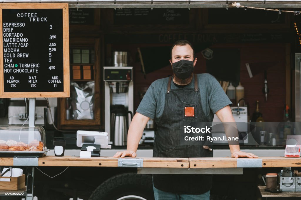 Food Truck Owner Wearing Protective Face Mask A mobile coffee truck is open for business during the Coronavirus pandemic.  The owner wears a mask during work hours. Food Truck Stock Photo