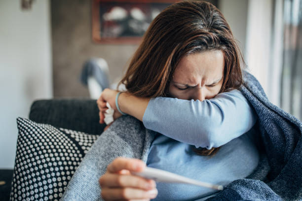 femme avec des symptômes de fièvre s’asseyant sur le sofa et retenant le thermomètre - pneumonia photos et images de collection