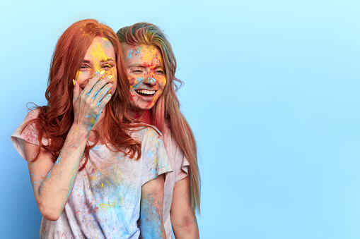 open your hearts and enjoy Holi.two friends laughing at their dirty friends, ginger girl with a palm on her mouth and her blonde sister watching the amazing holiday. copy space