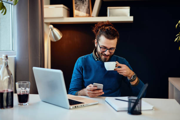 istock Young attractive bearded hipster sitting in his office, drinking coffee and using smart phone. 1226066573