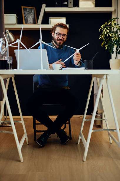 istock Young innovative caucasian bearded employee sitting in his office and holding windmill model. Sustainable development concept. 1226066914