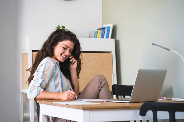 istock Smiling woman taking notes while talking on mobile phone stock photo 1226066948