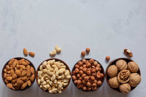 Nuts in wooden and clay bowls on a gray background with a copy space. Hazelnuts, cashews, almonds and walnuts. Flat lay.