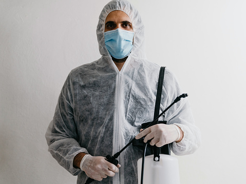 Portrait of a sanitation worker against a white background. He's holding crop sprayer for decontamination.