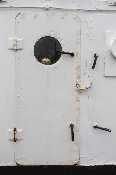 Ship door painted white with round porthole window, chained and padlocked, creative copy space, entry denied, vertical aspect