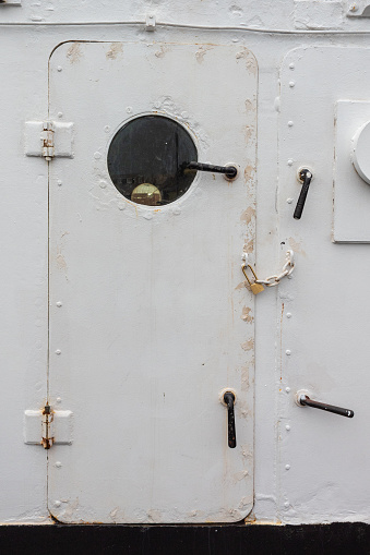 Ship door painted white with round porthole window, chained and padlocked, creative copy space, entry denied, vertical aspect