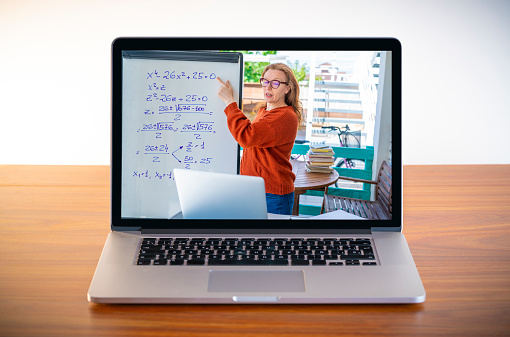 Female teacher teaching remotely her class from laptop screen on wooden table desk