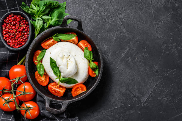 istock Caprese salad with burrata mozzarella, cherry tomatoes and Basil. Black background. Top view. Copy space 1226073790
