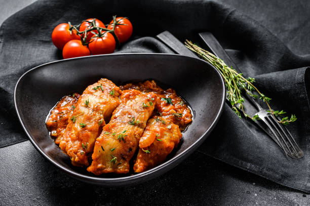 istock Baked Tilapia fish in tomatoes on a plate. Black background. Top view 1226076052