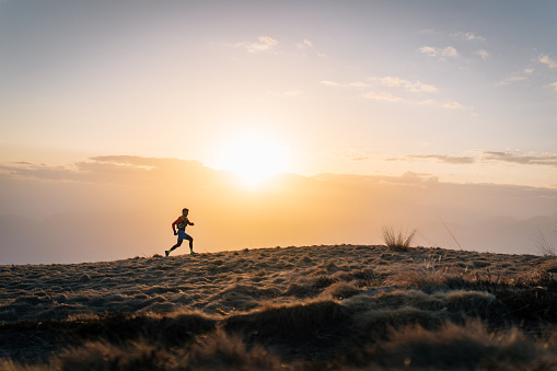 Young man trail runs up mountain at sunrise
