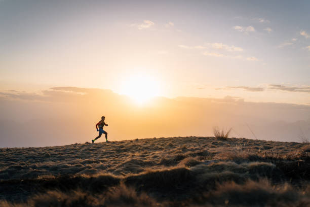 Young man trail runs up mountain at sunrise Mountain ranges in distance wellbeing photos stock pictures, royalty-free photos & images