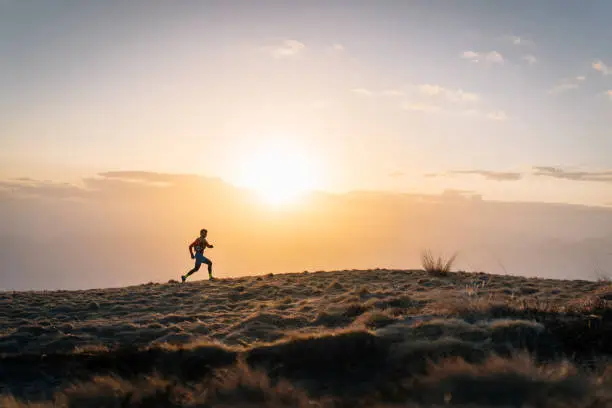 Photo of Young man trail runs up mountain at sunrise