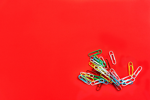 Stationery colorful paper clips chaotically scattered on a red background.