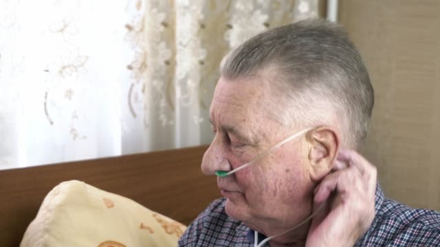 Elderly person puts a nasal catheter with oxygen on his head at home