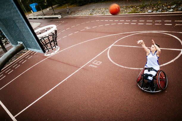 femme dans le fauteuil roulant jouant le basket-ball et marquant - sport et récréation d’incapacité - sports en fauteuil roulant photos et images de collection
