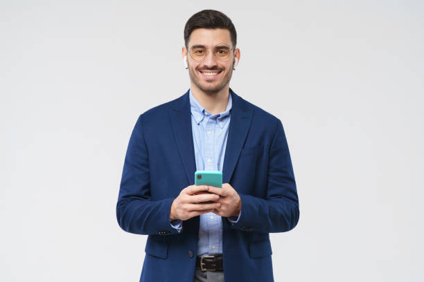 istock Business guy standing with smartphone in hands, looking at camera with happy confident smile, feeling relaxed, isolated on gray background 1226086658