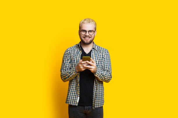 istock Blonde caucasian man is chatting with somebody using a phone while wearing eyeglasses on a yellow wall 1226086923