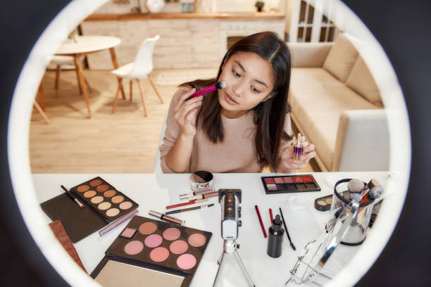 Makeup Inspired By You. Asian female blogger applying makeup while recording a tutorial video for her beauty blog using camera at home