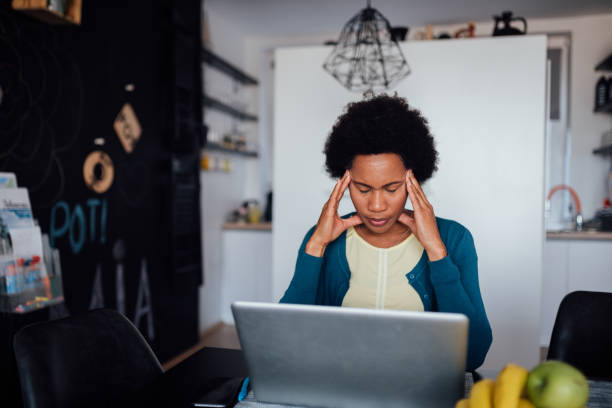 Young African American woman struggling to find a job Worried African American woman sitting at home unemployed, looking for a job using a laptop and struggling with the depression and dealing with a headache struggle photos stock pictures, royalty-free photos & images