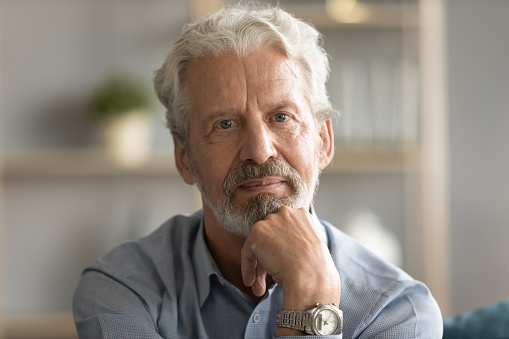 Portrait of thoughtful pondering middle aged hoary man touching chin, looking at camera. Head shot close up pensive mature old grandfather thinking of problems difficulties, retirement life concept.