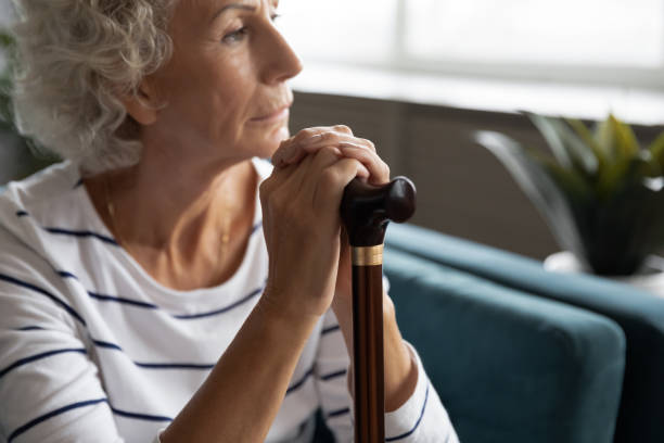 istock Thoughtful elder disabled woman sitting on sofa with wooden stick. 1226093735