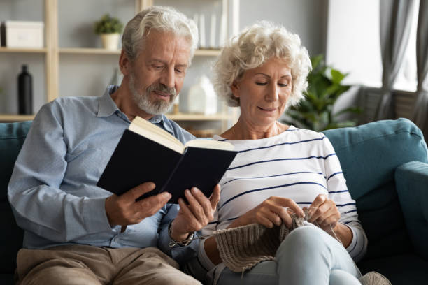 istock Happy mature husband reading book while smiling elderly wife knitting. 1226093745