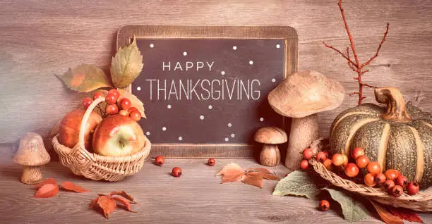 Text "Happy Thanksgiving" on blackboard. Autumn traditional decorations, toned panoramic image. Fall leaves, berries, mushrooms, pumpkins, flowers on wood. Thanksgiving still life.