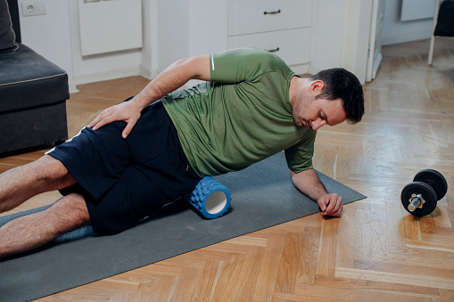 Fitness at home: a handsome man massaging his body with a blue foam roller.