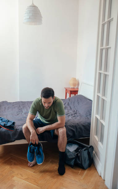 istock Workout Preparations at Home: a Fit Handsome Man Sitting on Bed and Putting on Socks and Sneakers to go Running (Copy Space) 1226096044